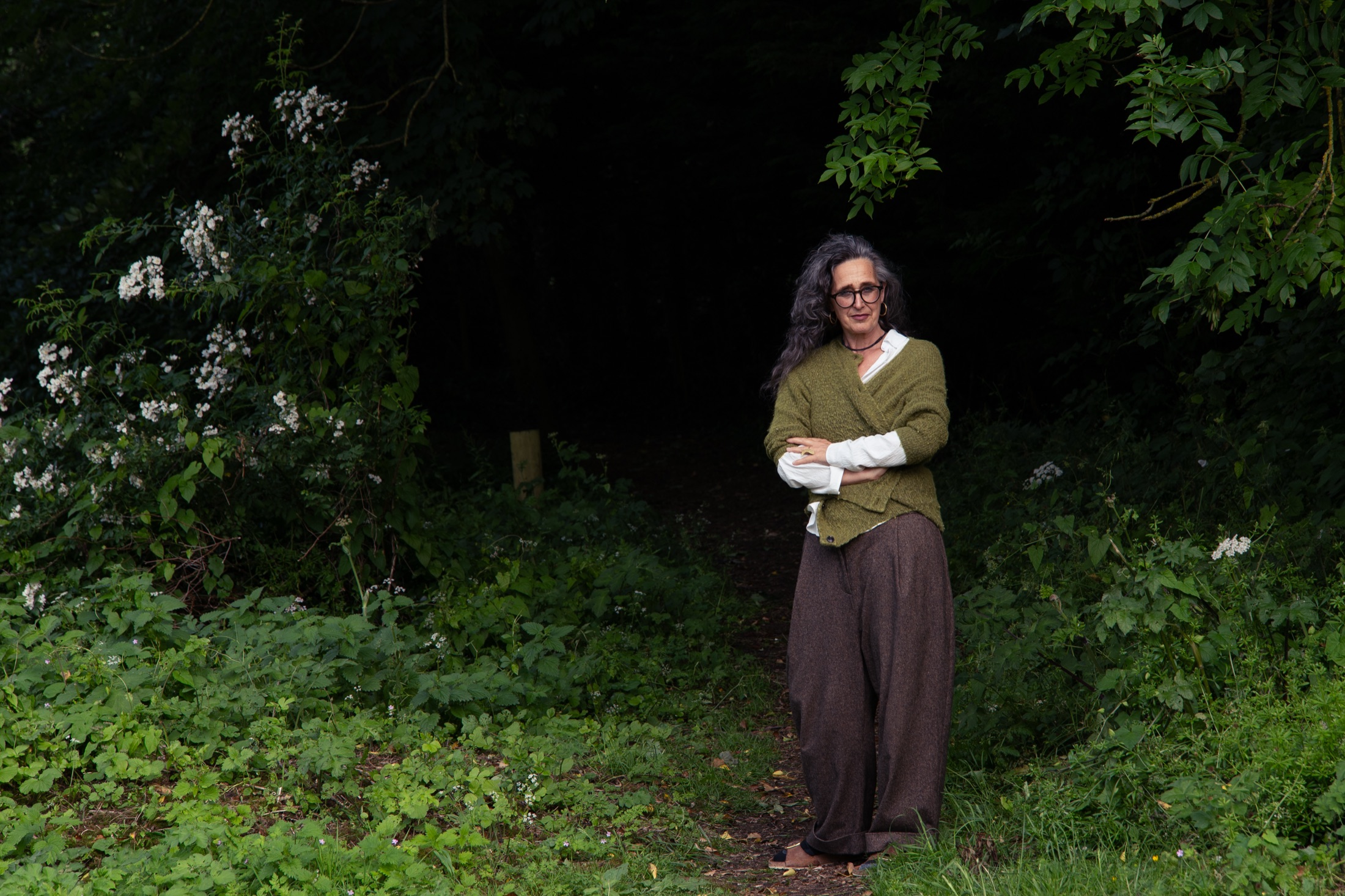 Christiane Churchill-Ley in a green cardigan standing among woodland foliage.